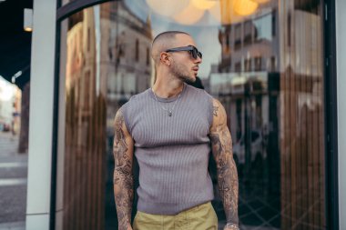 Kolunda dövmeleri ve şehirde poz veren yakışıklı sakallı adamın portresi.