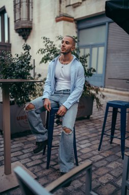 Sandalyede oturan kotlu, şık, genç ve yakışıklı bir adamın portresi.