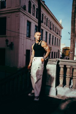 Beyaz pantolonlu ve güneş gözlüklü genç adam şehir sokaklarında poz veriyor.