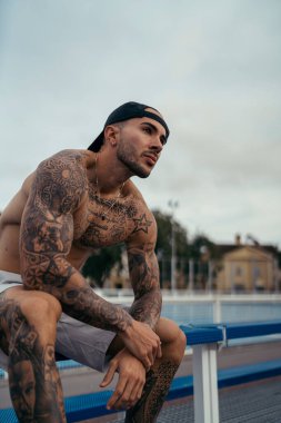 Şapkalı yakışıklı ve güneş gözlüklü adam merdivenlerde oturuyor.