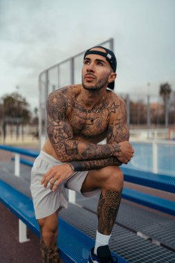 Spor şapkalı ve spor elbiseli yakışıklı bir adam şehir parkında dinleniyor..