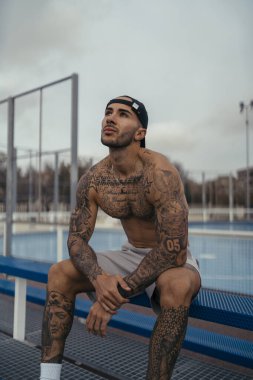 Spor salonundaki bankta oturan dövmeli genç yakışıklı bir sporcunun portresi..