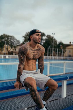 Suyun arka planında dövmesi olan yakışıklı, kaslı genç bir adam.