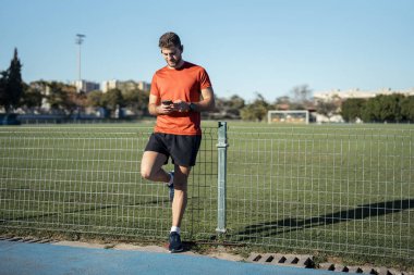 Spor giyim sektöründe yakışıklı sporcu parkta koşarken cep telefonuyla müzik dinliyor.