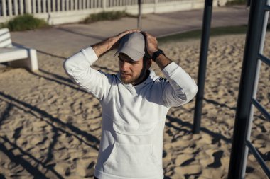 Genç adam plajda beyaz tişört giyiyor.