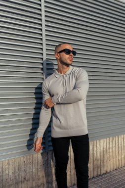 Güneş gözlüklü genç kaslı adam sokakta poz veriyor.