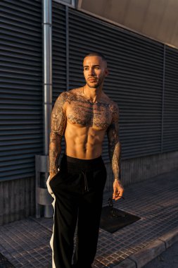 Spor kıyafetleri ve dövmeleri olan genç yakışıklı bir adam şehirde poz veriyor..