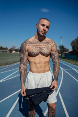 Parkta poz veren yakışıklı, kaslı genç bir sporcu.