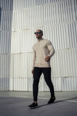 Güneş gözlüklü yakışıklı genç adam kentsel bağlamda poz veriyor.