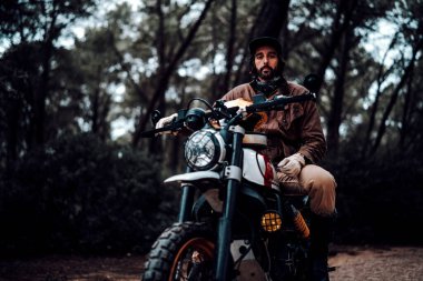 Ormanda oturan kasklı ve siyah ceketli genç adam..