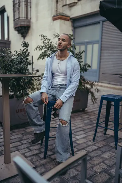 Sandalyede oturan kotlu, şık, genç ve yakışıklı bir adamın portresi.