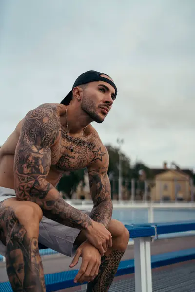 Şapkalı yakışıklı ve güneş gözlüklü adam merdivenlerde oturuyor.