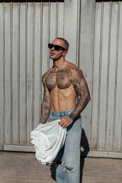 Vücudunda güneş gözlüklü dövme olan genç bir adamın portresi.