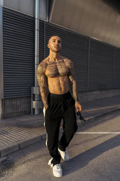 Siyah tişörtlü, beyaz şortlu, sırtında büyük bir dövme olan genç ve yakışıklı bir adam..