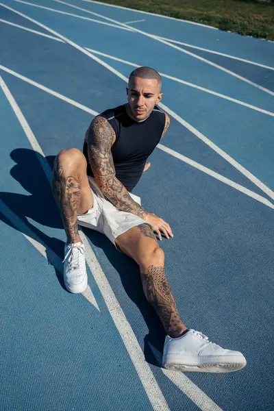 Spor elbiseli genç adam parkta antrenmandan sonra dinleniyor, kameraya bakıyor.