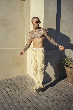 Dövmeli adam duvarın önünde poz veriyor.