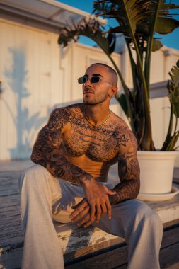 Parktaki bankta oturan güneş gözlüklü yakışıklı bir gencin portresi.