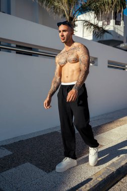 Dövmeli, beyaz bluzlu yakışıklı ve kaslı bir genç adam.