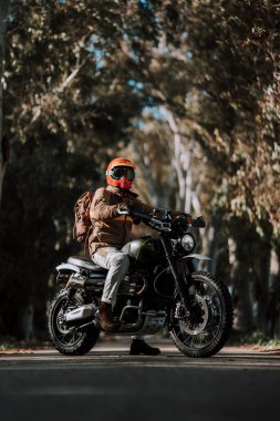 Sırtında kaskla motosiklet süren, deri ceketli ve güneş gözlüklü bir adam..