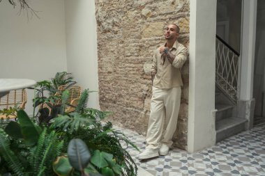 Beyaz gömlekli ve güneş gözlüklü genç bir turist apartmanın balkonunda poz veriyor.