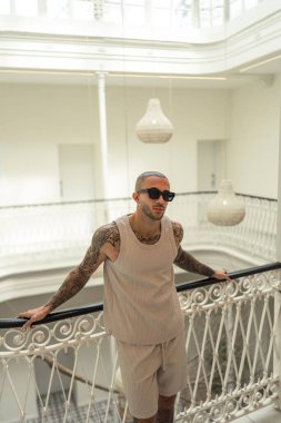 Beyaz tişörtlü bir adam apartmanın koridorunda poz veriyor.