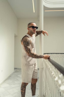 Pencerenin yanında duran dövmeli genç adam.