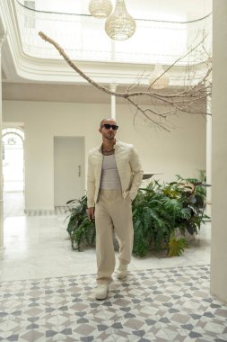 Beyaz gömlekli, güneş gözlüklü ve beyaz önlüklü genç bir adam şehirde yürüyor.