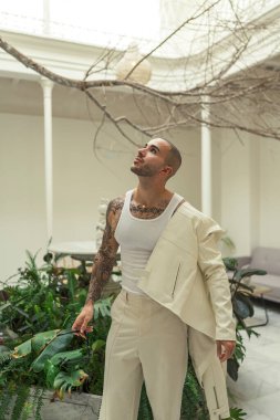 Şık takım elbiseli, beyaz gömlekli, otelin içinde bitkisi olan yakışıklı bir adam..