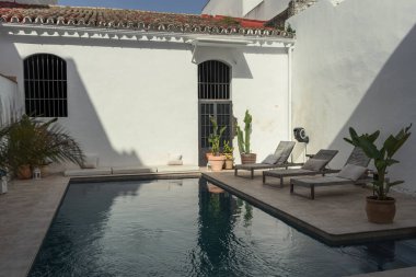 Boş bir terası ve beyaz bir duvarı olan bir yüzme havuzu manzarası.