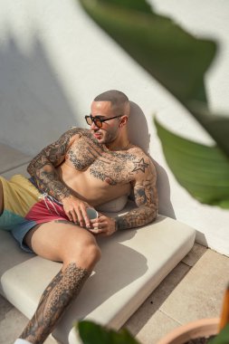 Dövmeli bir adam dinleniyor ve içki içiyor..