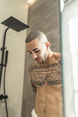 Sabahları banyoda dikilirken aynaya bakan üstsüz bir adam.