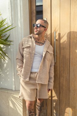 Güneş gözlüklü şık adam tahta arka planda poz veriyor.