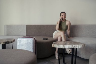 Beyaz elbiseli genç bir kadın bir kafede oturuyor ve telefonla konuşuyor.
