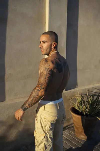 Beyaz tişörtlü çekici bir erkeğin dikey pozu bir duvarın arkasında.