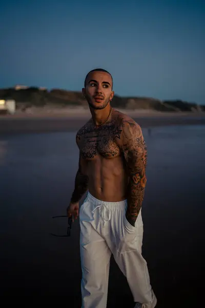 Kumsalda dövmeleri olan yakışıklı bir adamın portresi.