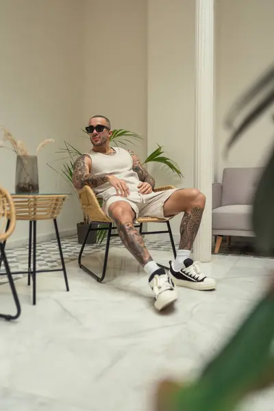 Adam gündelik giysiler içinde elinde kahveyle sandalyede oturuyor..