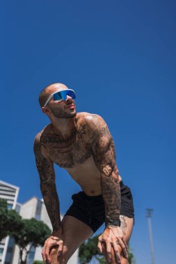 Dövmeli yakışıklı kaslı adam binanın önünde poz veriyor.