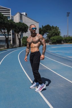 Güneş gözlüklü ve siyah spor giysili yakışıklı stadyumda duruyor..