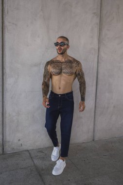 Dövmeleri ve dövmeleri olan yakışıklı genç bir erkek şehir merkezinde poz veriyor.