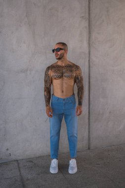 Kaslı vücutlu, beyaz bluzlu ve şehir ortamında poz veren yakışıklı bir genç.