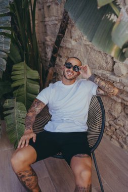 Günlük giysiler ve güneş gözlüğü takan genç adam oturma odasında dinleniyor.