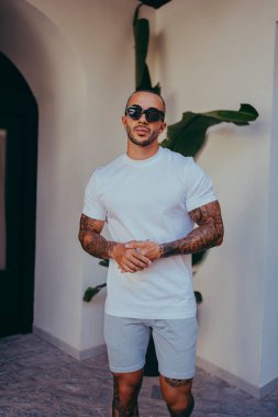 Beyaz tişörtlü genç yakışıklı şehirde poz veriyor.