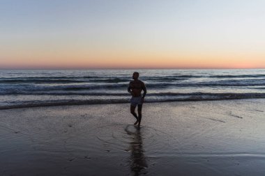 Genç adam deniz kıyısında yürüyor. gün batımı