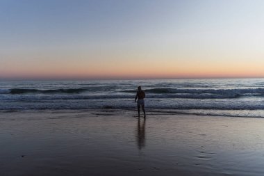 Gün doğumunda sahilde yürüyen adam.