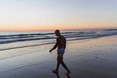 Beyaz sakallı genç bir adam gün batımında sahil boyunca yürür. Adam sporla meşgul. Spor ve sağlık kavramı.