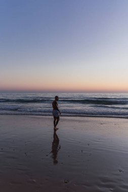 Gün doğumunda sahilde yürüyen bir adam.