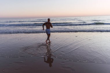 Gün batımında plajda koşan siyah tişörtlü bir adam..