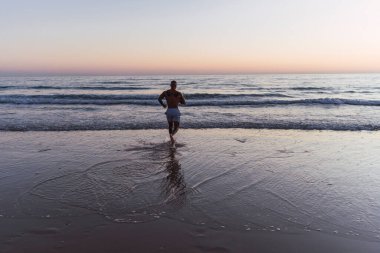 Genç adam güneşin doğuşuyla denizde koşuyor..