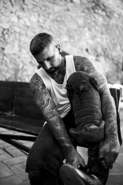 Dövmeli bir arabada yerde oturan bir adam..