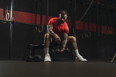 Genç adam spor salonunda dambılla antrenman yapıyor.